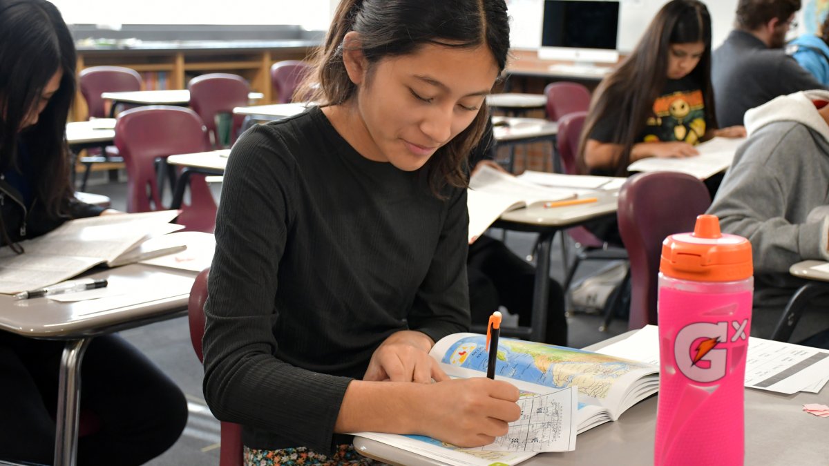 student writing with a map book open on her desk