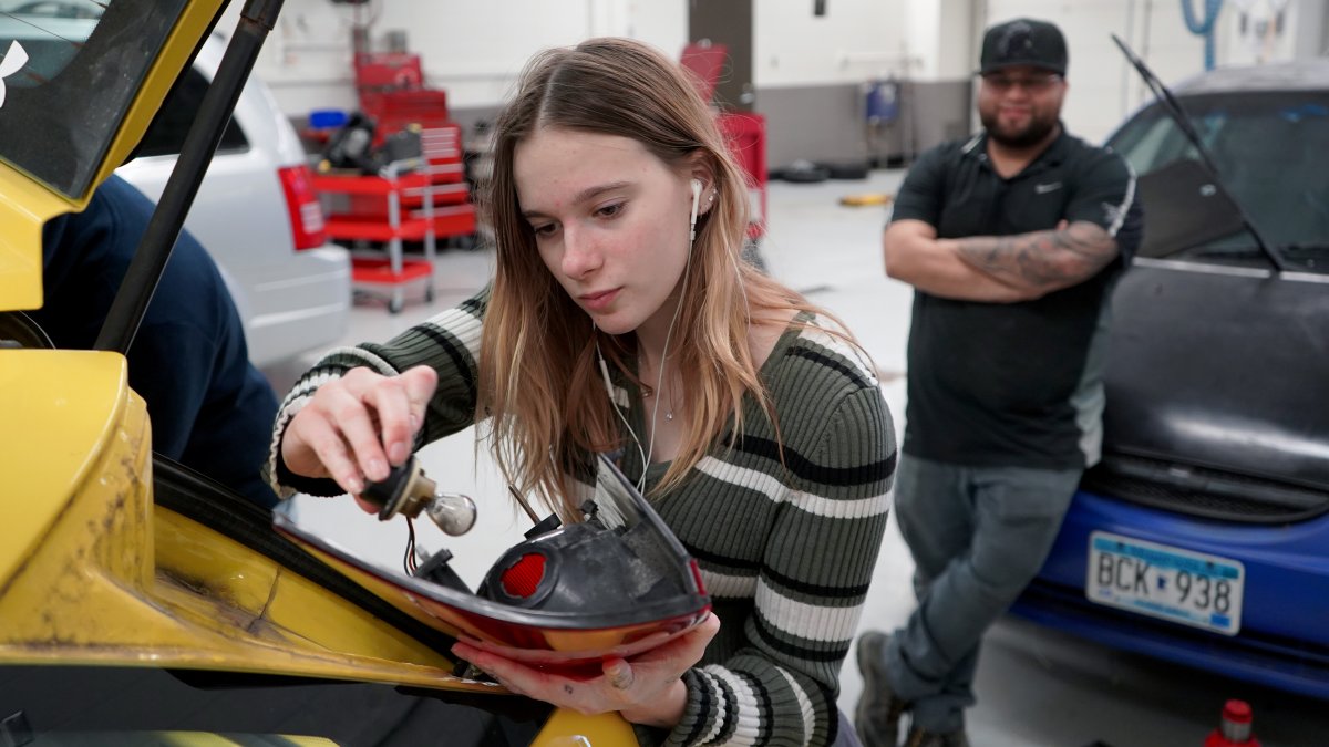 Female high school student working on car in shop class