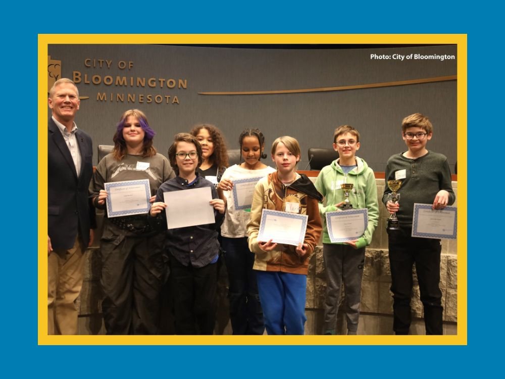 Seven middle school students holding certificates with Bloomington Mayor Tim Busse